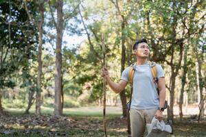 Young man asian trekking among trees with backpack, young man enjoy alone in forest. Camping, hiking, travelling, search for adventure concept photo