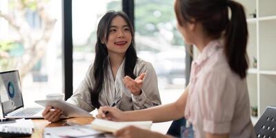 Two Asian businesswoman working with laptop computer and discussing documents and idea at meeting. Teamwork process photo