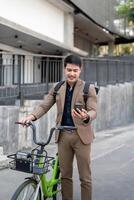 Asian businessman in a suit is riding a bicycle on the city streets for his morning commute to work. Eco transportation concept, sustainable lifestyle concept photo