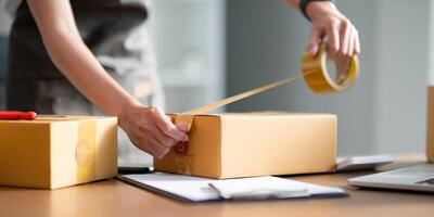 Woman use scotch tape to attach parcel box to prepare goods for the process of packaging, shipping, online sale internet marketing ecommerce concept startup business idea photo