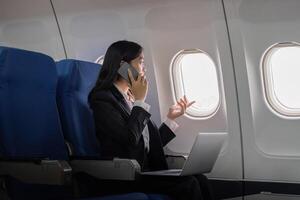 exitoso joven asiático negocio mujer se sienta en avión cabina avión y trabajando desde en cualquier lugar. volador a primero clase foto