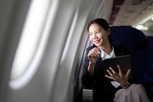 Successful young asian business woman sits in airplane cabin plane and working from anywhere. Flying at first class photo