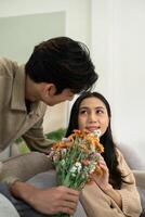 Romantic young asian couple embracing with holding flowers and smiling in living room at home. fall in love. Valentine concept photo