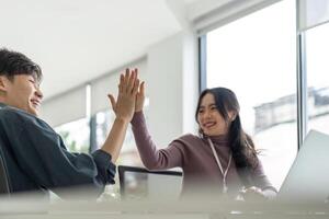 Successful business people giving each other a high five in a meeting. Two young business celebrating teamwork in an office photo