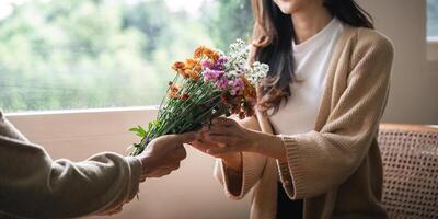 Romantic young asian couple embracing with holding flowers and smiling in living room at home. fall in love. Valentine concept photo