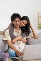Happy asian couple using laptop sit relax on sofa doing ecommerce shopping online on website at home photo