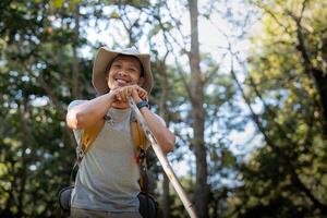 Young man asian trekking among trees with backpack, young man enjoy alone in forest. Camping, hiking, travelling, search for adventure concept photo