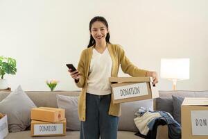 Donation concept. Woman asian holding a donate box with full of clothes. Woman holding clothes donate box. Clothes in box for concept donation and reuse recycle photo