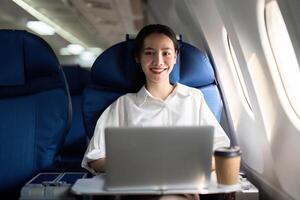 exitoso joven asiático negocio mujer se sienta en avión cabina avión y trabajando desde en cualquier lugar. volador a primero clase foto