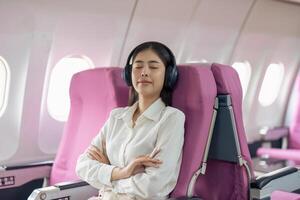 asiático mujer en cabina vistiendo auricular descansando mientras escuchando a música en avión durante vuelo foto