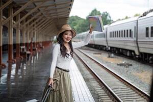 Alone Asian woman traveler with suitcase in train station platform. Summer vacation holiday and travel concept photo