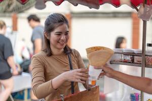 contento joven asiático viajero Conocedor gourmet mujer orden crepes a al aire libre noche mercado calle comida vendedor foto