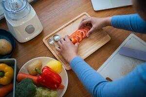 mujer es cocinar en hogar cocina. hembra manos cortar Tomates en mesa en de madera tableros estilo de vida momento foto