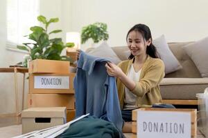 Woman asian holding donation box full with clothes and select clothes. Concept of donation and clothes recycling. Helping poor people photo