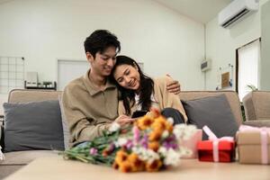 Asian couple lifestyle using phones, shopping or chatting online, sitting on couch at home, holding smartphones, enjoy leisure time. fall in love. Valentine concept photo