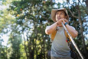 Young man asian trekking among trees with backpack, young man enjoy alone in forest. Camping, hiking, travelling, search for adventure concept photo