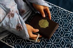 A Muslim woman sitting on a prayer mat and holding the quran with Indonesian translation photo