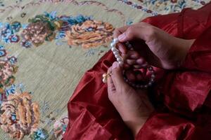 A Muslim woman wearing a moslem clothes with hijab called mukena and holding prayer beads for praying or dhikr photo