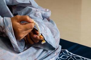 A Muslim woman wearing a moslem clothes with hijab called mukena and holding prayer beads for praying or dhikr photo