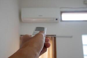 Hand holding AC remote control directed on the air conditioner inside the room photo