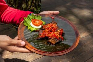 Hands holding a wooden plate of beef fried Lungs with Spicy Red Sauce or Paru Goreng Balado photo