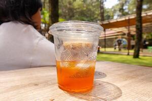 un Fresco hielo té en para llevar taza en el mesa con naturaleza antecedentes foto