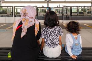 un musulmán madre con su dos hijas sentado en el banco a Jacarta mrt tren estación. esperando para el tren a llegar. foto