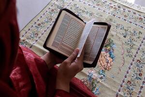 A Muslim woman sitting on a prayer mat and reading the quran with Indonesian translation photo