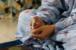 A Muslim woman wearing a moslem clothes with hijab called mukena and holding prayer beads for praying or dhikr photo