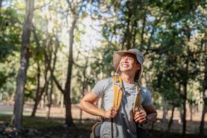 Young man asian trekking among trees with backpack, young man enjoy alone in forest. Camping, hiking, travelling, search for adventure concept photo