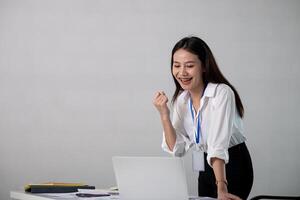 Happy excited business woman in office working with computer make winner gesture. excited success business asian woman triumph in office photo