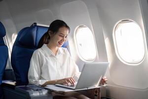 Successful young asian business woman sits in airplane cabin plane and working from anywhere. Flying at first class photo