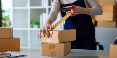 Woman use scotch tape to attach parcel box to prepare goods for the process of packaging, shipping, online sale internet marketing ecommerce concept startup business idea photo