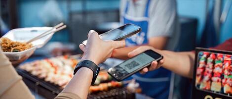 Asian traveler paying contactless with mobile phone in street food night market. Mobile payment concept photo