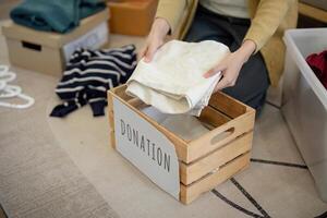 donación, asiático joven mujer sentado paquete objeto a hogar, poniendo en cosas dentro donar caja con segundo mano ropa, caridad Ayudar y necesitado gente. reutilizar reciclar foto