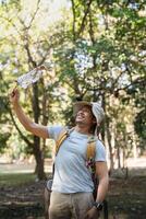 Young man asian trekking among trees with backpack, young man enjoy alone in forest. Camping, hiking, travelling, search for adventure concept photo