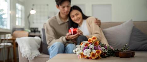 Romantic young asian couple embracing with holding flowers and smiling in living room at home. fall in love. Valentine concept photo