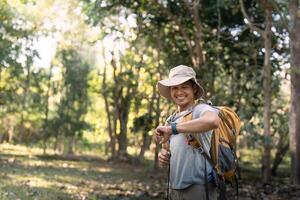 Young man asian trekking among trees with backpack, young man enjoy alone in forest. Camping, hiking, travelling, search for adventure concept photo