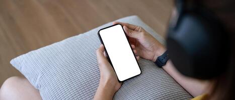 Bosquejo teléfono inteligente de un mujer participación móvil teléfono con blanco blanco pantalla mientras sentado escucha a música a hogar foto