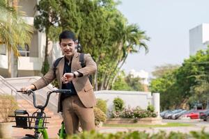 Asian businessman in a suit is riding a bicycle on the city streets for his morning commute to work. Eco transportation concept, sustainable lifestyle concept photo