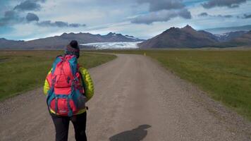 fêmea turista com mochila vai de sujeira estrada em fundo do montanhas e geleira dentro Islândia. liberdade e viagem conceito. 4k video
