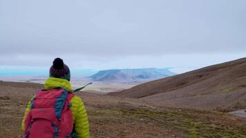 uma mulher com uma vermelho mochila viaja dentro a montanhas do Islândia. liberdade e viagem conceito. 4k video