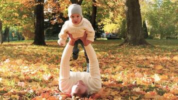 Portrait of a happy family resting in the autumn forest. Dad picks up his son in his arms while lying down on blanket. Horizontal video