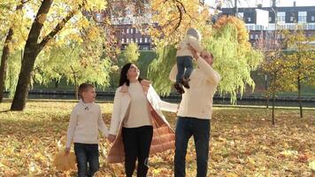 A happy family of four spend time in the autumn park. Family walking in the park and enjoying a sunny day. Horizontal photo video