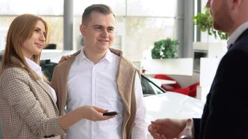 Male dealer passing car keys to happy couple and shaking hand of satisfied client. Auto business, car sale, technology and people concept video