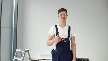 joven Maestro en trabajo uniforme y con un conjunto de herramientas soportes en un blanco pared antecedentes video