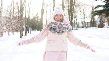 vrouw slagen sneeuw. jong vrouw in een zacht roze naar beneden jasje slagen sneeuw in voorkant van de camera Aan een achtergrond van besneeuwd landschap video