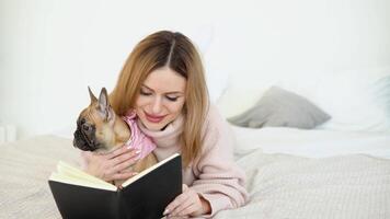 un mujer en un acogedor polvo rosado suéter y blanco medias acostado en el cama con su perro y lee un libro video