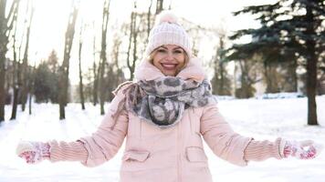 donna colpi neve. giovane donna nel un' morbido rosa giù giacca colpi neve nel davanti di il telecamera su un' sfondo di nevoso paesaggio video
