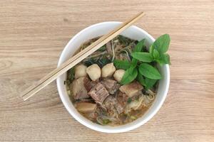 Asian Pork noodle soup with meatball and fresh vegetable on wood background. photo